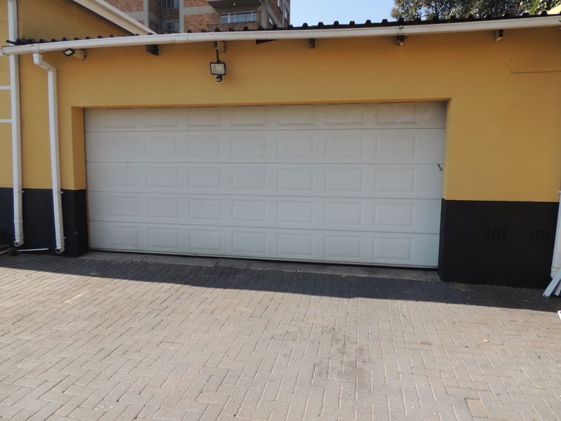 A functional garage featuring a white sectional door, paved driveway access, and external security lighting.