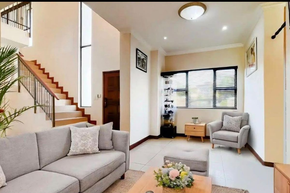 A bright and spacious living room featuring tiled floors, a modern staircase with a metal balustrade, and large windows allowing for natural light.