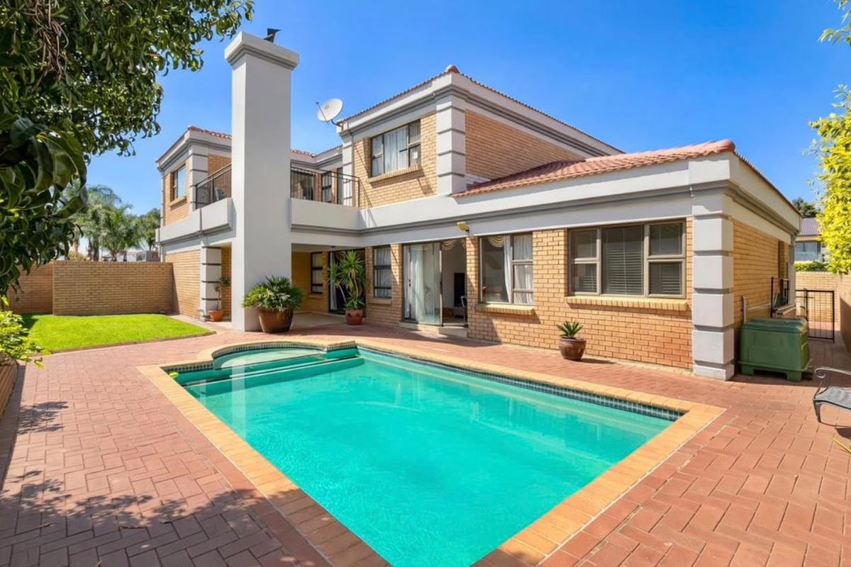 Rear view of a two-story brick house featuring a swimming pool, paved patio area, and an upper-level balcony.