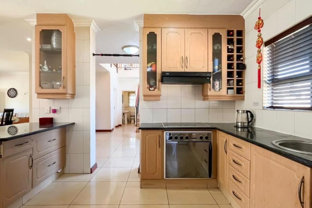 A functional kitchen featuring light wood cabinetry, granite countertops, built-in oven, hob, and tiled finishes, offering a practical layout with ample storage space.