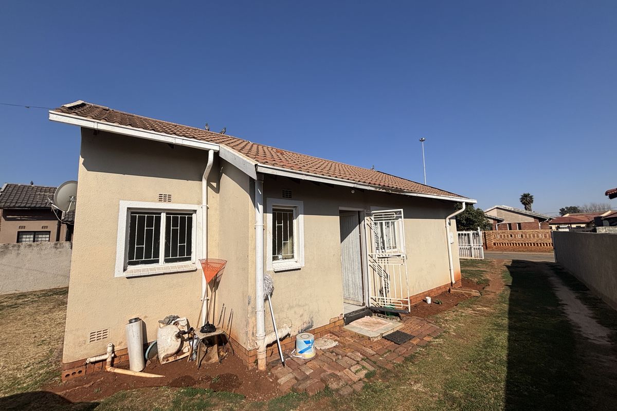 Rear view of the house showing the exterior facade, tiled roof, security features, and surrounding yard area.