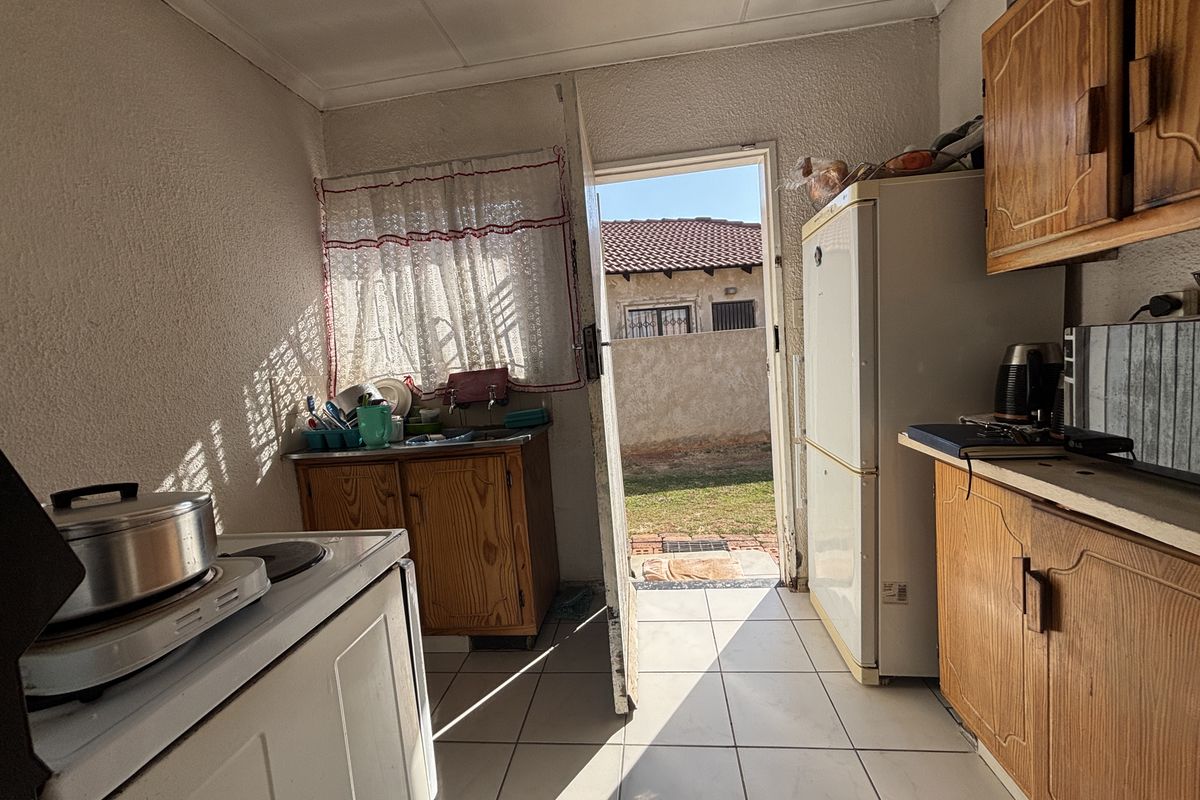 A functional kitchen featuring built-in wooden cabinetry, tiled flooring, and direct access to the rear garden area.