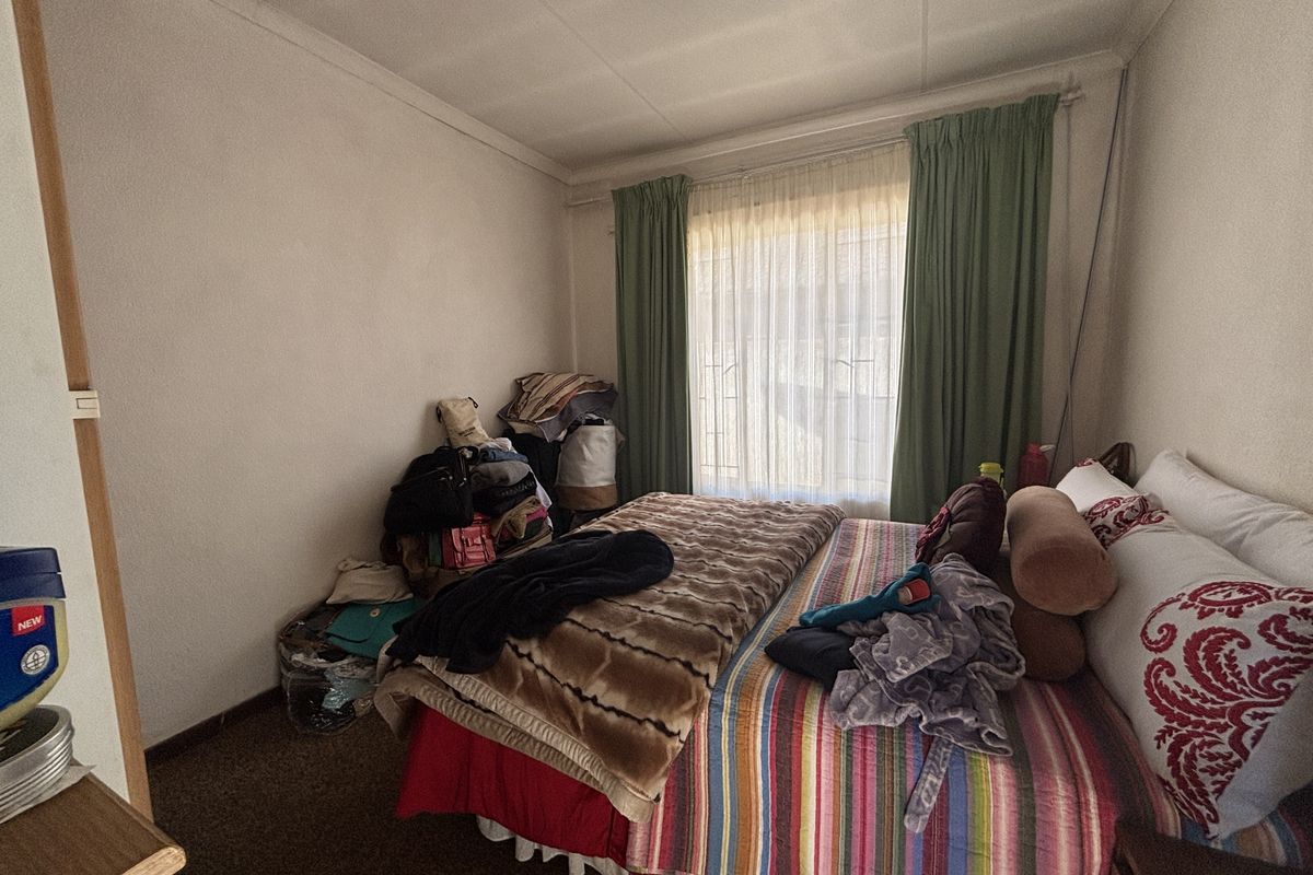 A standard bedroom featuring carpeted flooring, window security bars, and curtain rails, offering a functional space ready for modernization.