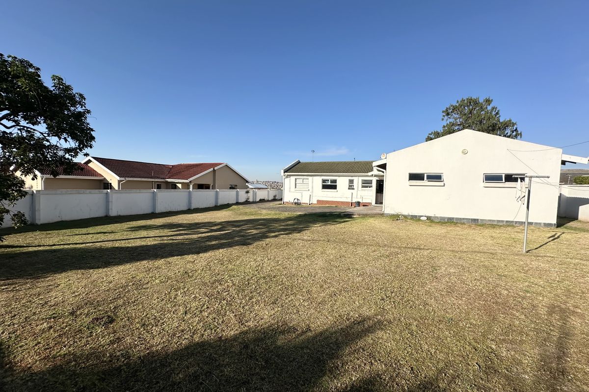 Spacious rear garden featuring a large lawn area, perimeter boundary walls, and a view of the rear building elevation.