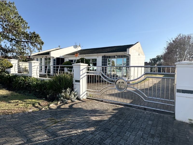 Front view of a single-story house featuring a secure stainless steel driveway gate, paved driveway, and well-maintained boundary wall with electric fencing.