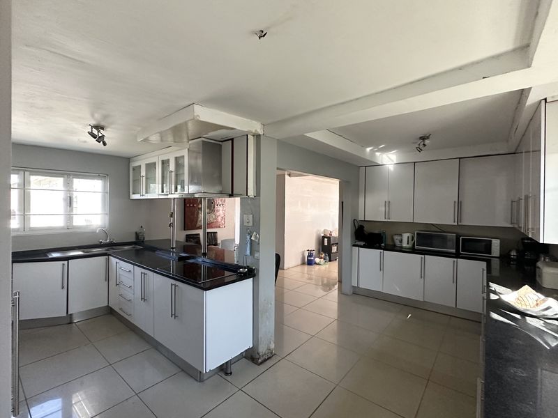 Spacious kitchen featuring white cabinetry, dark granite countertops, and tiled flooring, with an open-plan layout connecting to adjacent living areas.