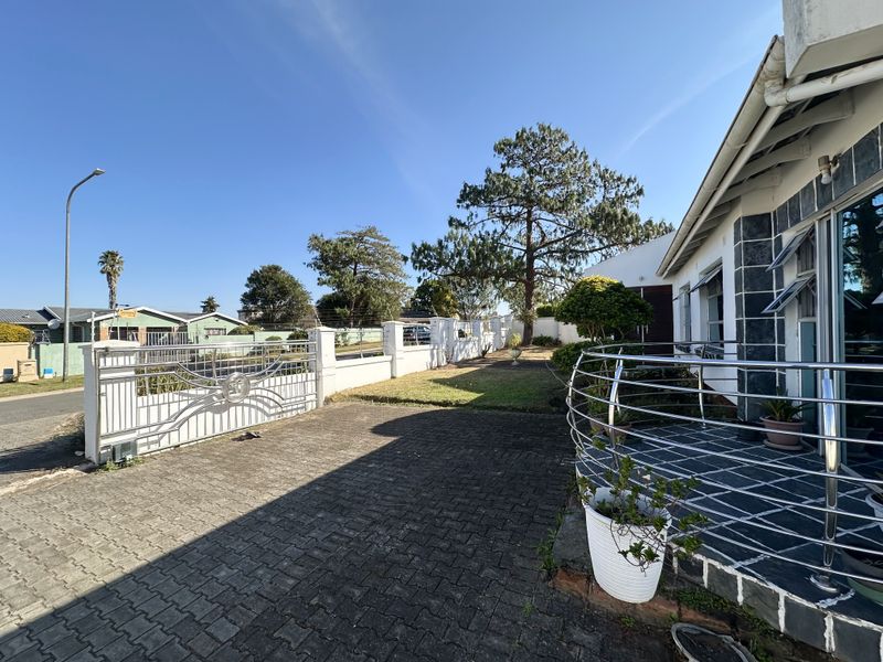 Front exterior view featuring a paved driveway, perimeter wall with metal gate, and a covered patio area with stainless steel balustrades.