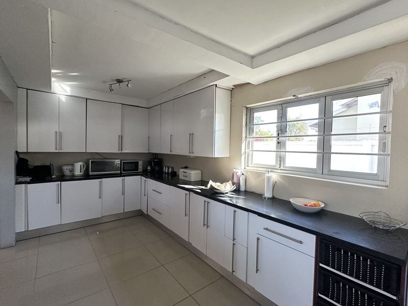 A functional kitchen featuring white cabinetry, dark countertops, and tiled flooring, currently requiring minor finishing work around the window area.