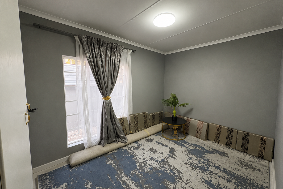 A neutrally painted bedroom featuring grey walls, a large window with curtain rod, and a central ceiling light fixture.