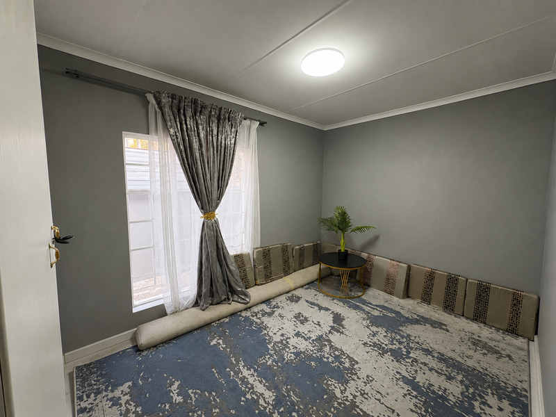 A neutrally painted bedroom featuring grey walls, a large window with curtain rod, and a central ceiling light fixture.