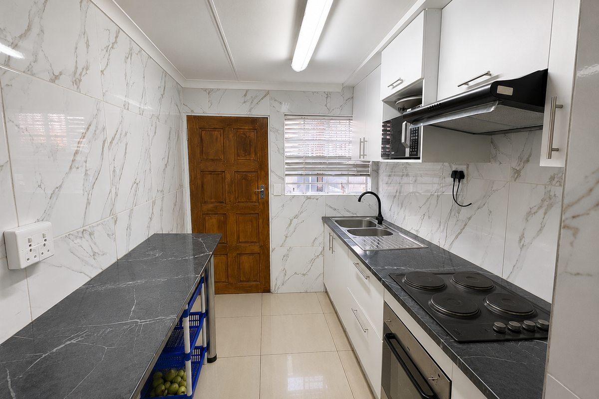 A functional kitchen featuring marble-look wall tiles, dark stone-look countertops, built-in cabinetry, an electric hob, and an integrated oven.