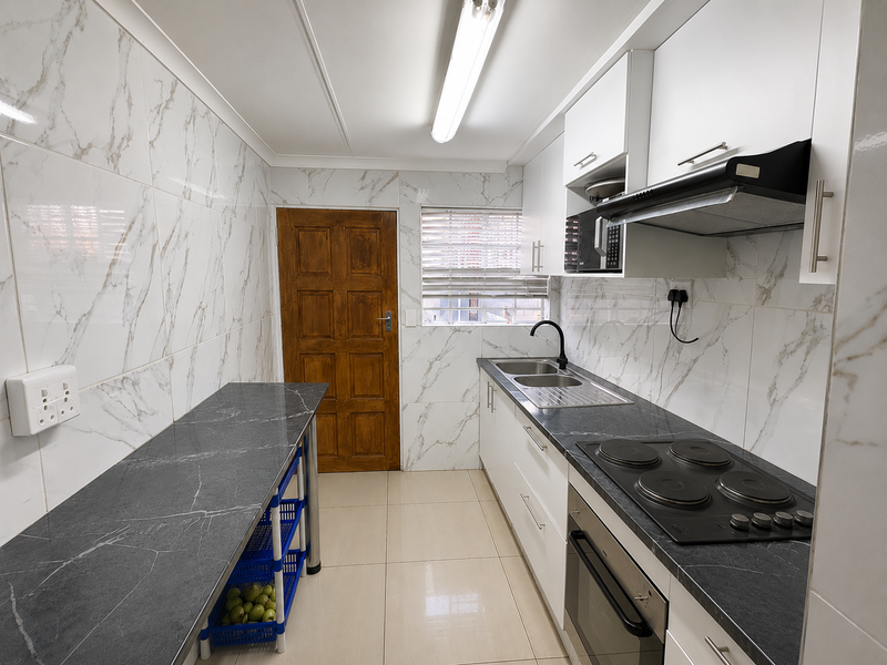 A functional kitchen featuring marble-look wall tiles, dark stone-look countertops, built-in cabinetry, an electric hob, and an integrated oven.