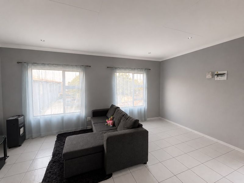 A bright living room featuring neutral grey walls, white tiled flooring, and recessed downlighting, offering a clean and functional space.