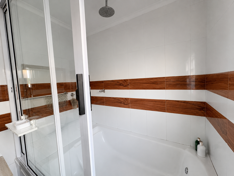 A clean bathroom featuring a built-in bathtub with a glass shower enclosure and modern white and wood-look tiled wall accents.