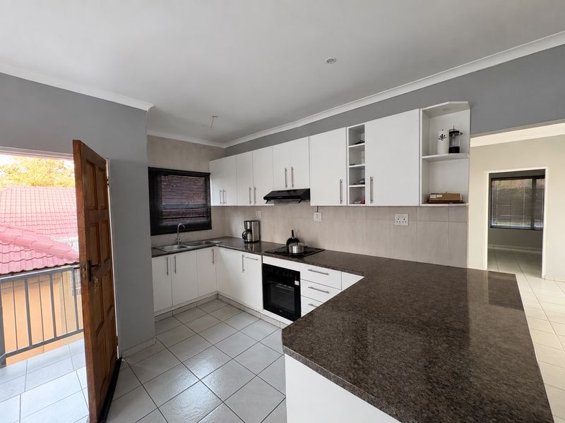 A functional kitchen featuring white cabinetry, granite countertops, built-in oven, hob, extractor fan, and tiled flooring with direct access to an outdoor balcony.