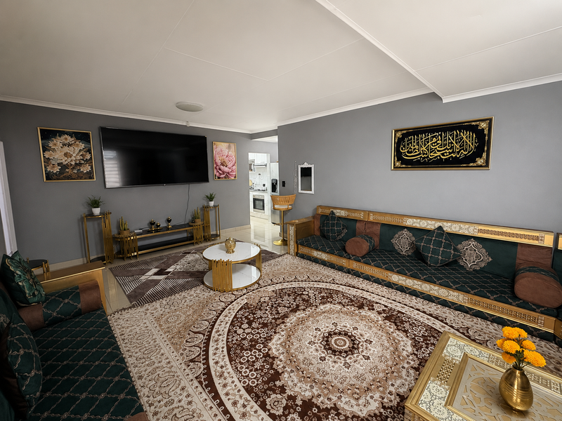 A well-maintained living room featuring neutral grey walls, tiled flooring, and decorative coving, with an open transition to the kitchen area.