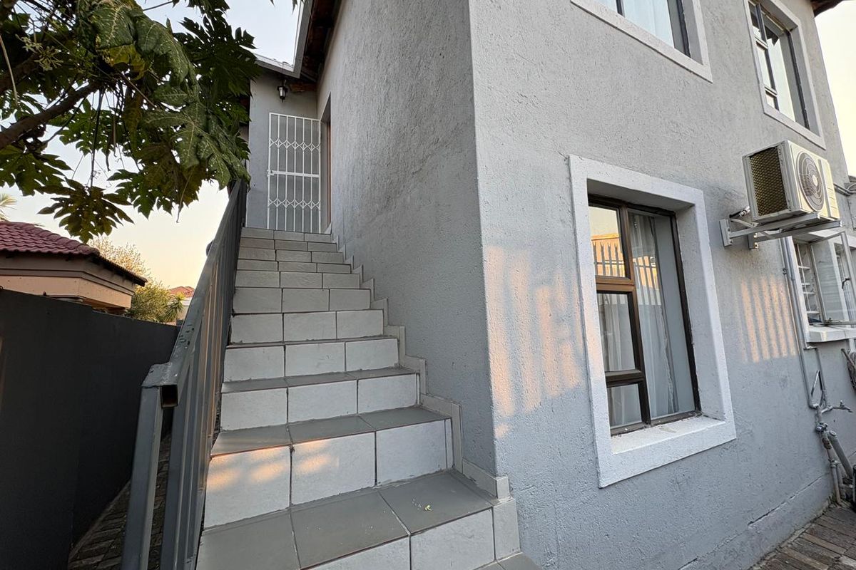 Exterior view of the property featuring a tiled staircase leading to an upper entrance, complemented by aluminium window frames and an external air conditioning unit.
