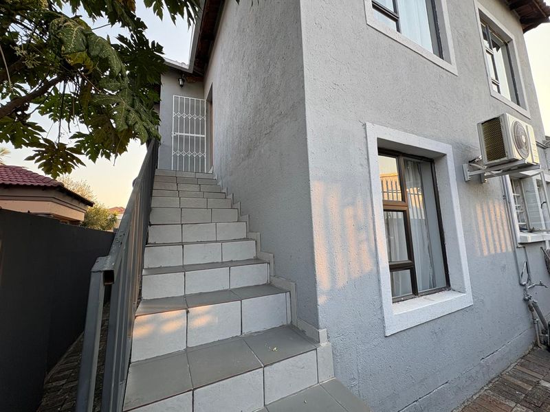 Exterior view of the property featuring a tiled staircase leading to an upper entrance, complemented by aluminium window frames and an external air conditioning unit.