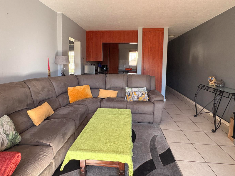 Open-plan living area featuring tiled flooring and a view through to the kitchen with built-in cabinetry.