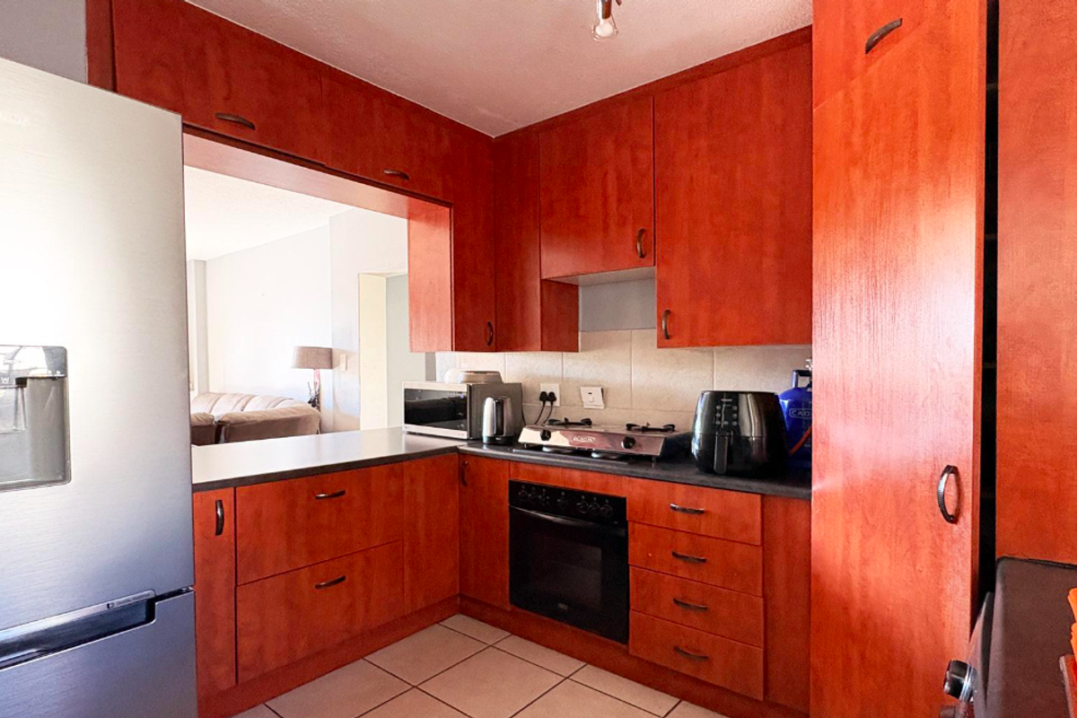 A functional kitchen featuring warm-toned wooden cabinetry, dark laminate countertops, a built-in oven, gas hob, and a convenient pass-through window to the living area.