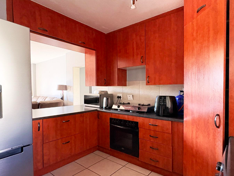 A functional kitchen featuring warm-toned wooden cabinetry, dark laminate countertops, a built-in oven, gas hob, and a convenient pass-through window to the living area.