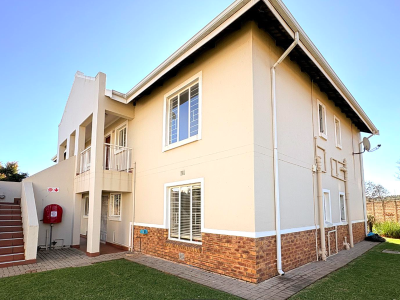 Rear view of a two-story townhouse featuring a brick-base facade, external staircase, balcony, and well-maintained surrounding lawn and paved pathways.