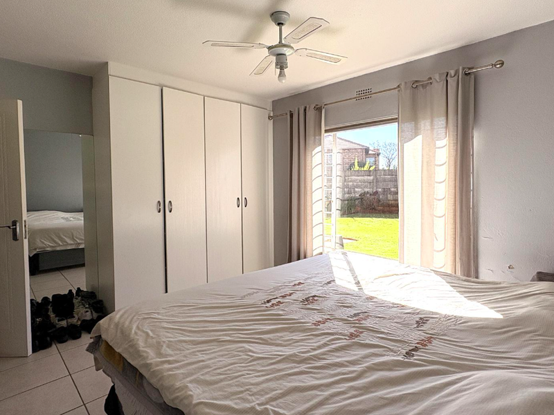 A bedroom featuring built-in cupboards, tiled flooring, a ceiling fan, and a sliding door providing direct access to the rear garden.