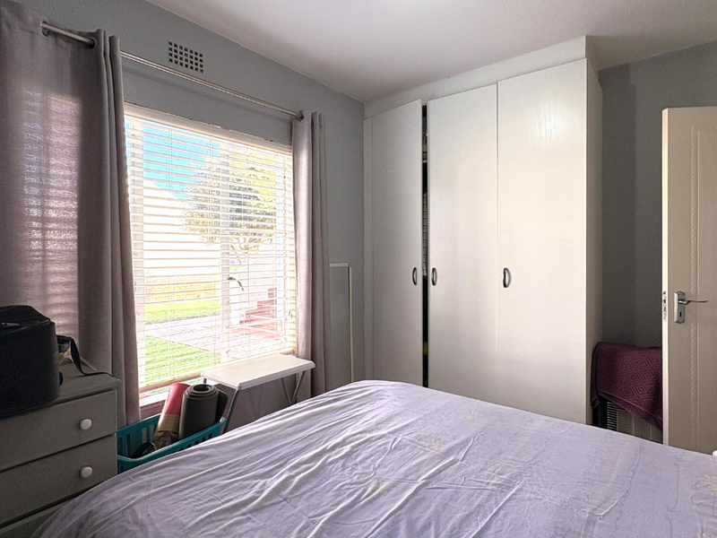 A functional bedroom featuring a built-in wardrobe, neutral wall tones, and natural light through a window with blinds.