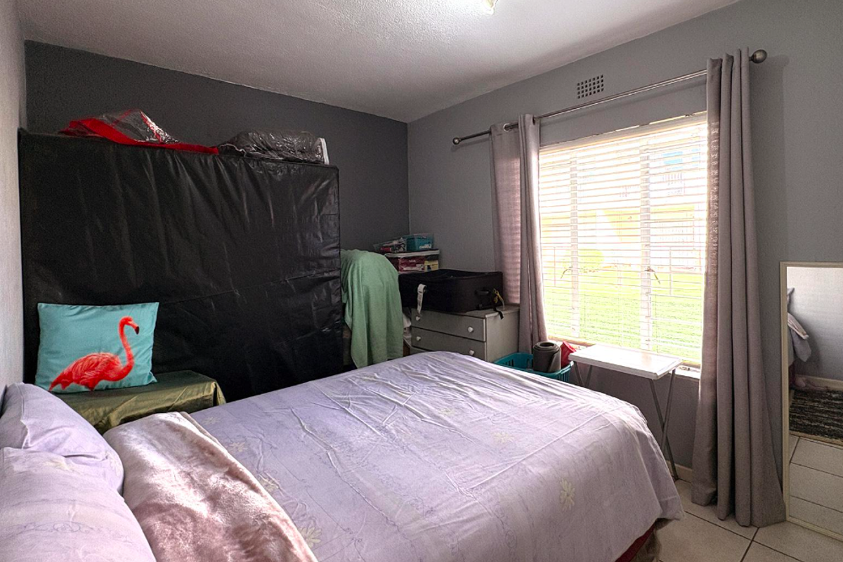 A standard bedroom featuring tiled flooring, a window with venetian blinds, and a curtain rod, providing a functional space for rest.