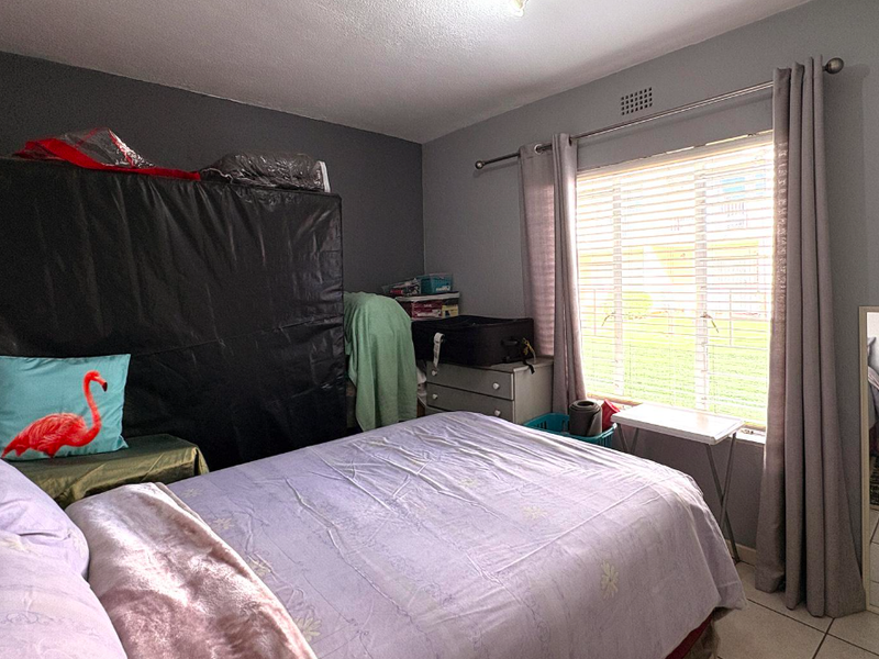 A standard bedroom featuring tiled flooring, a window with venetian blinds, and a curtain rod, providing a functional space for rest.