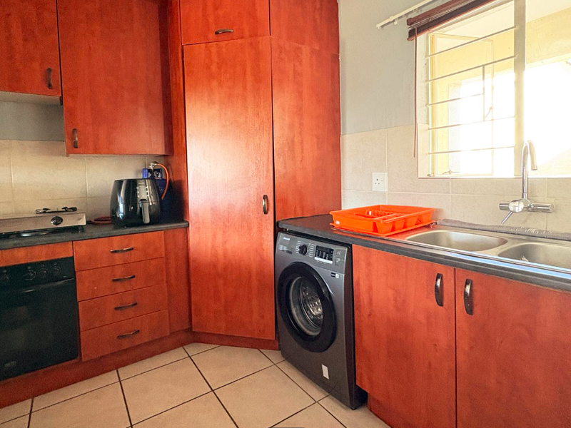 A functional kitchen featuring wooden cabinetry, laminate countertops, a double bowl sink, built-in oven, and gas hob with tiled flooring.