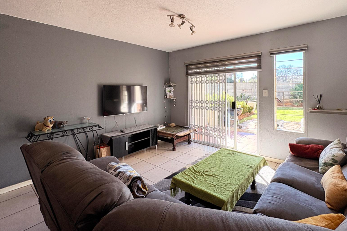 A comfortable living room featuring tiled flooring, a sliding glass door with security gate, and direct access to the rear garden area.