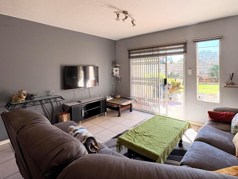 A comfortable living room featuring tiled flooring, a sliding glass door with security gate, and direct access to the rear garden area.