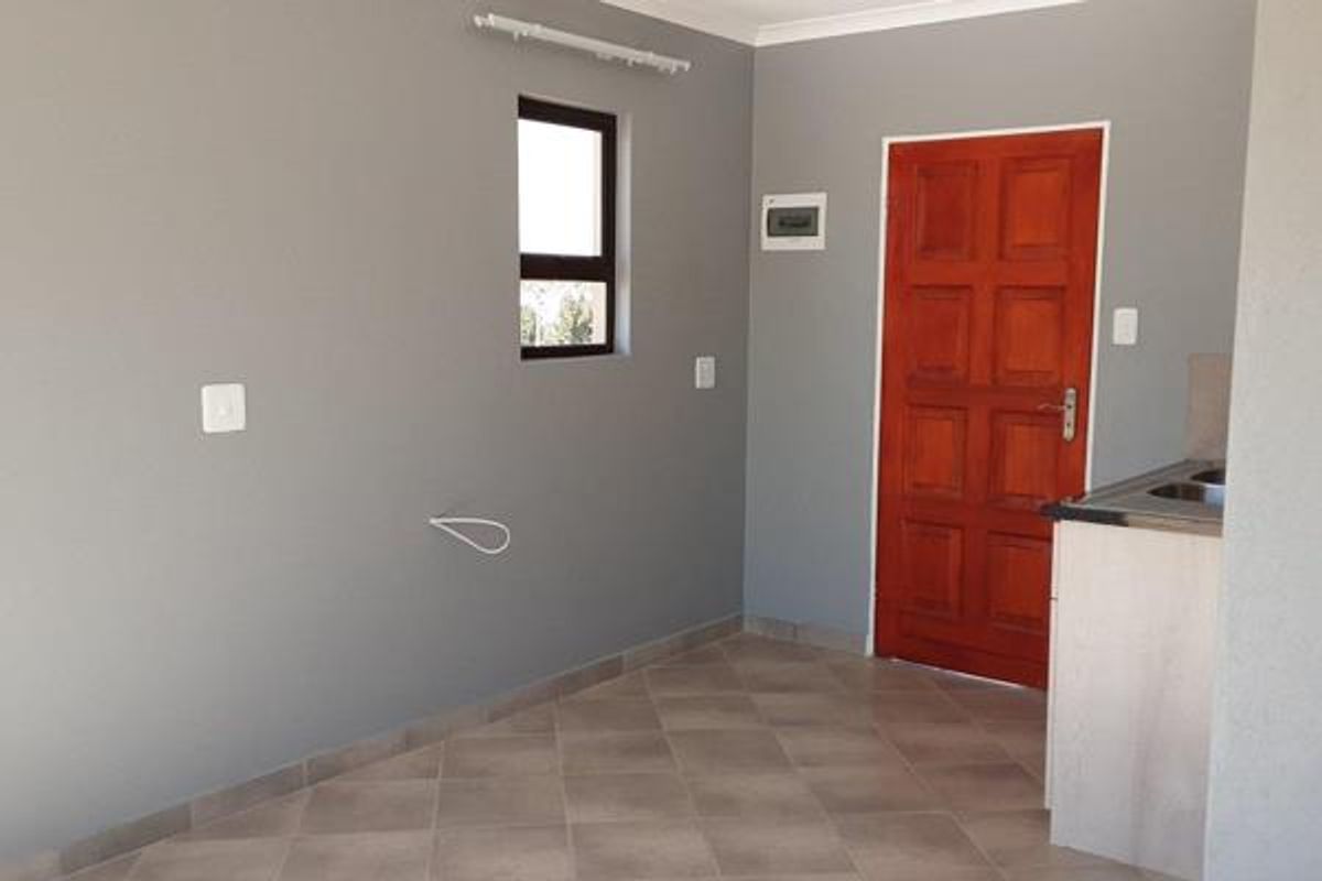 A clean, empty kitchen area featuring tiled flooring, neutral grey walls, a timber door, and basic cabinetry with a sink.