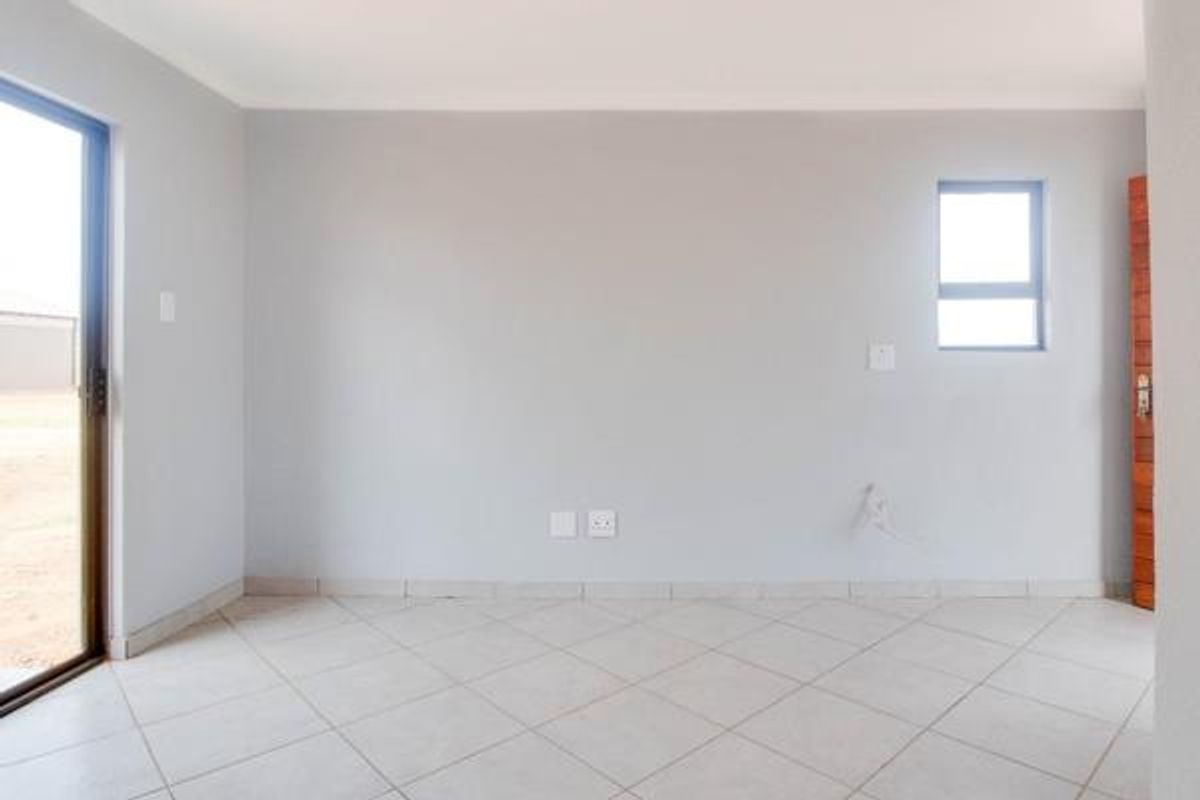A bright, empty living area featuring neutral walls, tiled flooring, and a sliding glass door providing access to the exterior.