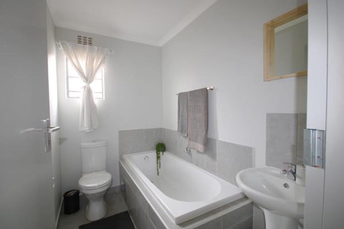 A clean and functional bathroom featuring a white bathtub, pedestal basin, and toilet with neutral grey wall tiling.