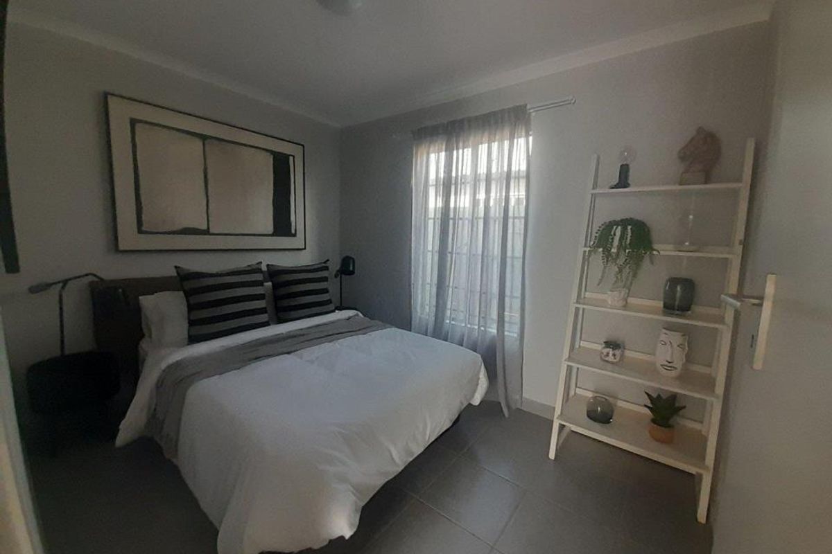A well-maintained bedroom featuring neutral wall tones, tiled flooring, and a window with sheer curtains, providing a comfortable and functional living space.