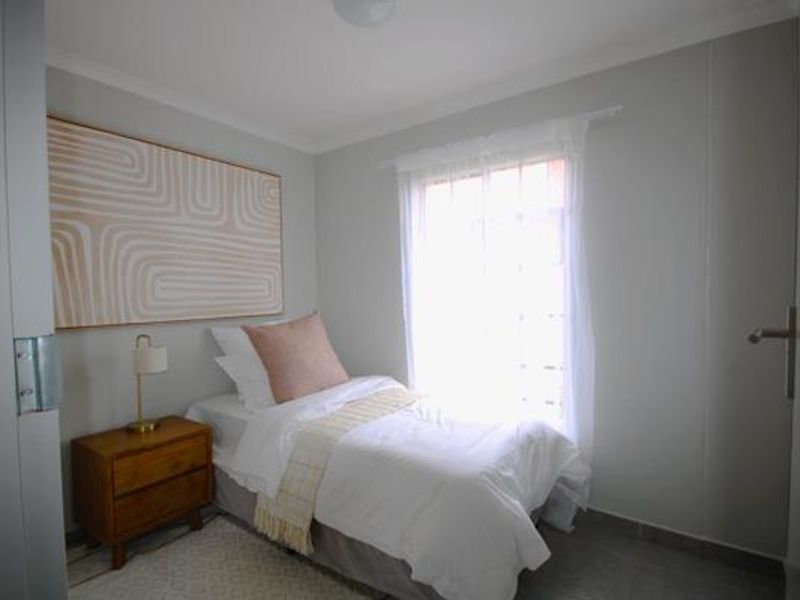 A compact bedroom featuring neutral wall tones, tiled flooring, and natural light through a window.