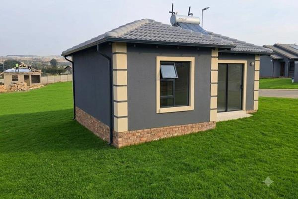 A modern detached residential structure featuring a dark grey facade with contrasting quoins, a solar water heating system, and a well-maintained lawn.