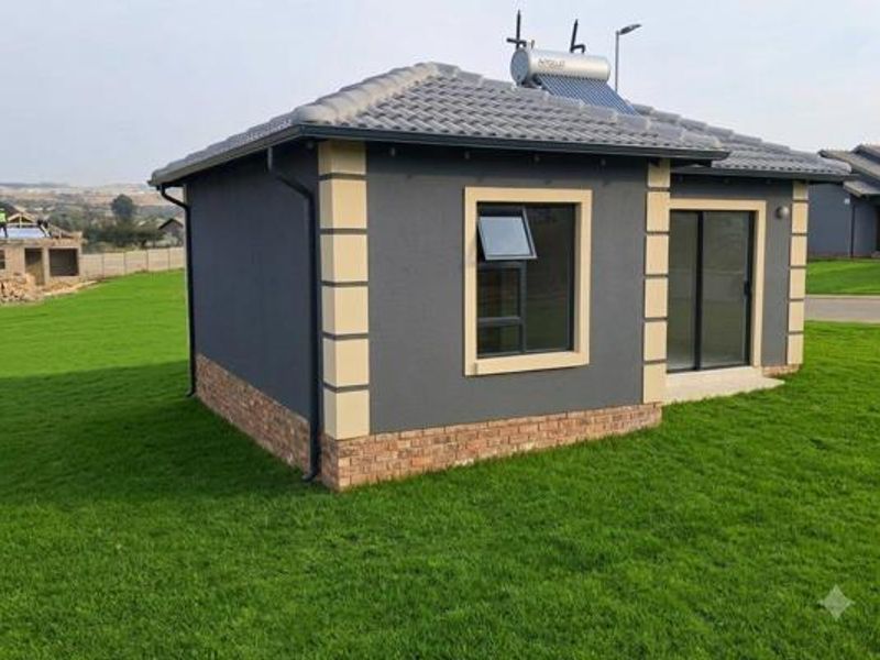 A modern detached residential structure featuring a dark grey facade with contrasting quoins, a solar water heating system, and a well-maintained lawn.