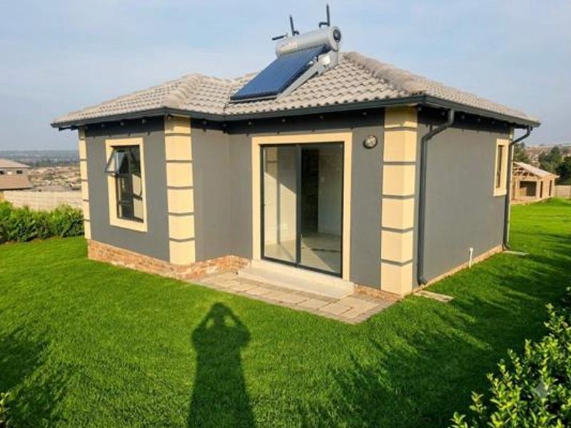 Rear view of a modern house featuring a solar water heater, tiled roof, sliding glass door, and well-maintained lawn.