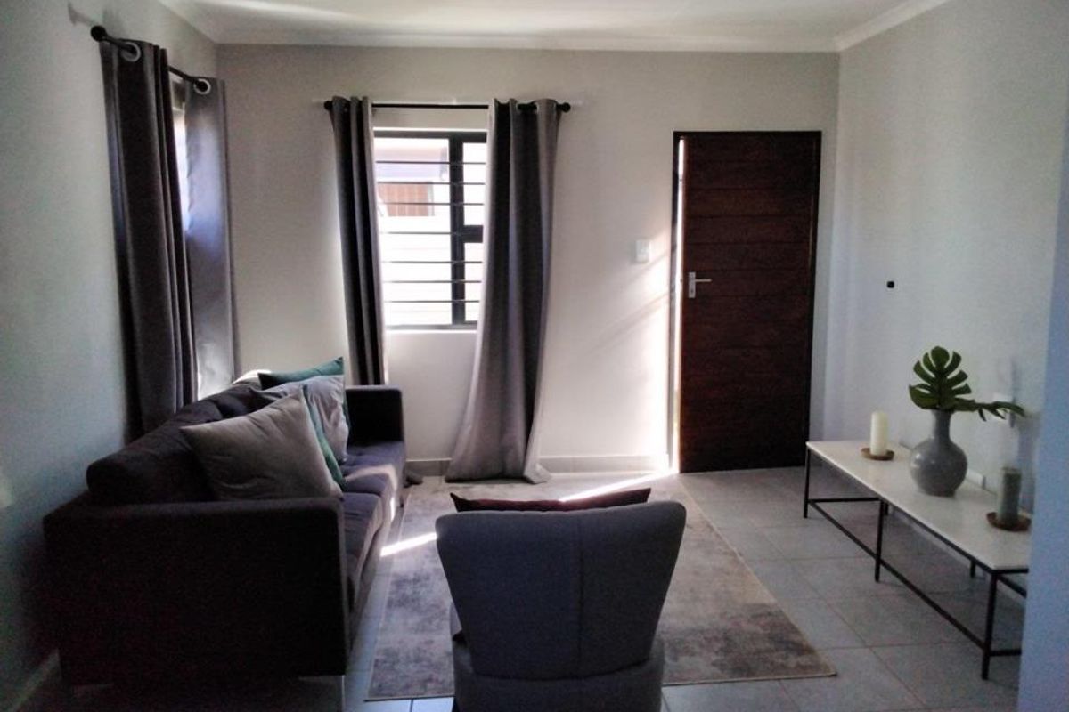 A well-lit living room featuring neutral tiled flooring, a secure window with burglar bars, and a solid timber entrance door.