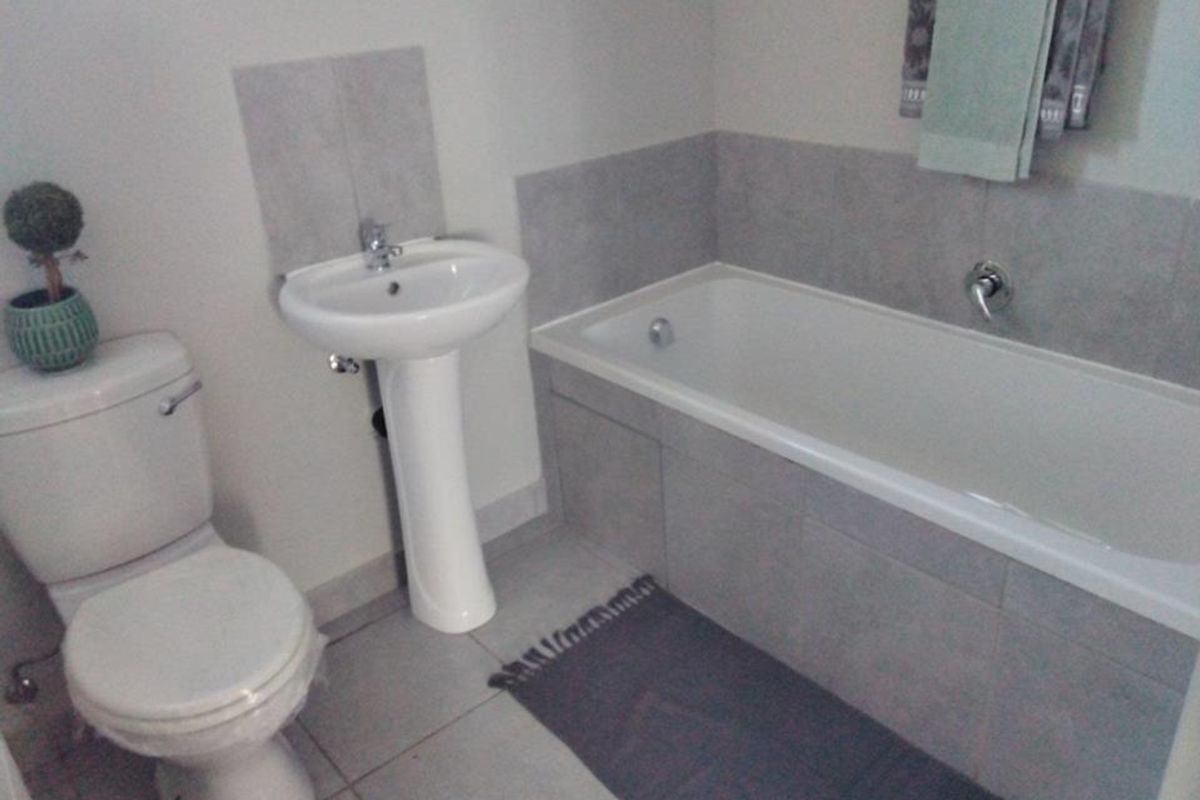 A functional bathroom featuring a pedestal basin, a built-in bathtub with wall tiling, and neutral ceramic floor tiles.