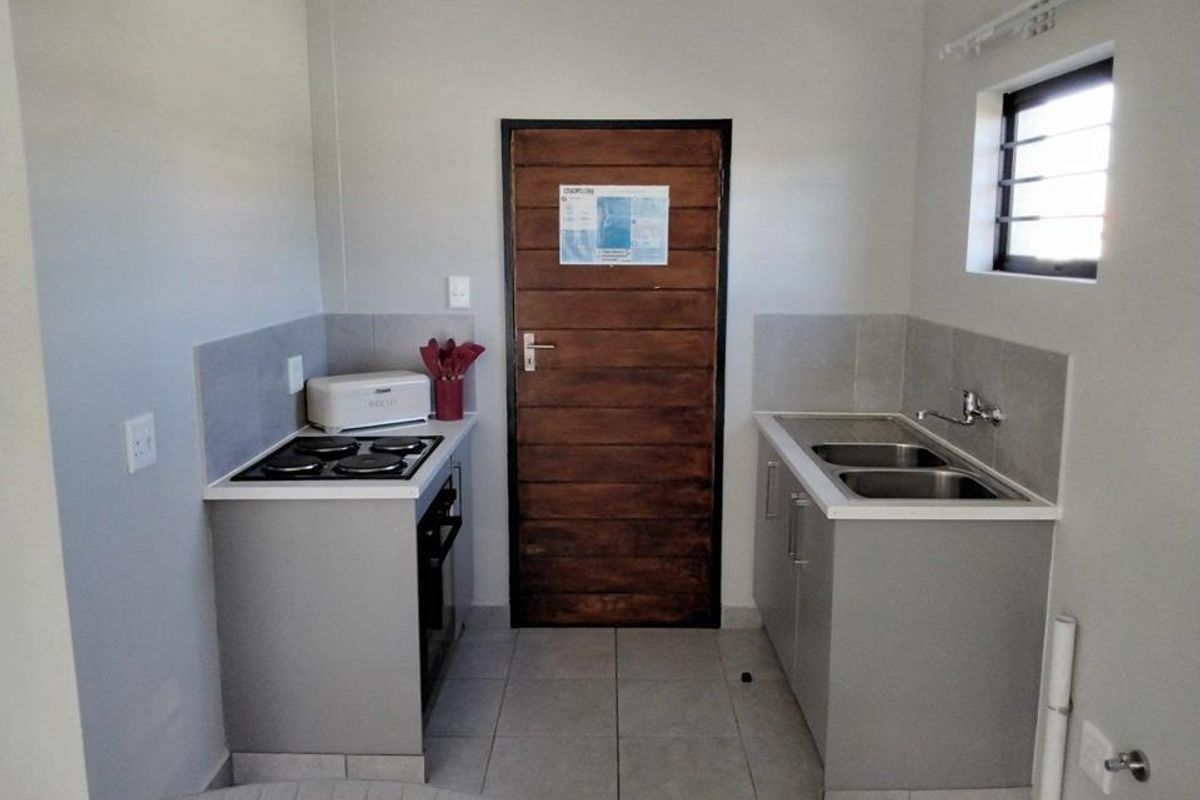 Compact kitchen featuring built-in cabinetry, a double sink, a stove with oven, and tiled splashbacks, providing a functional and efficient workspace.