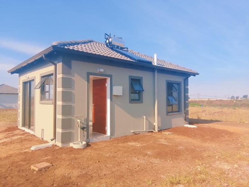 Rear view of a modern detached house featuring a solar water heating system, tiled roof, and aluminium window frames on a developing plot.