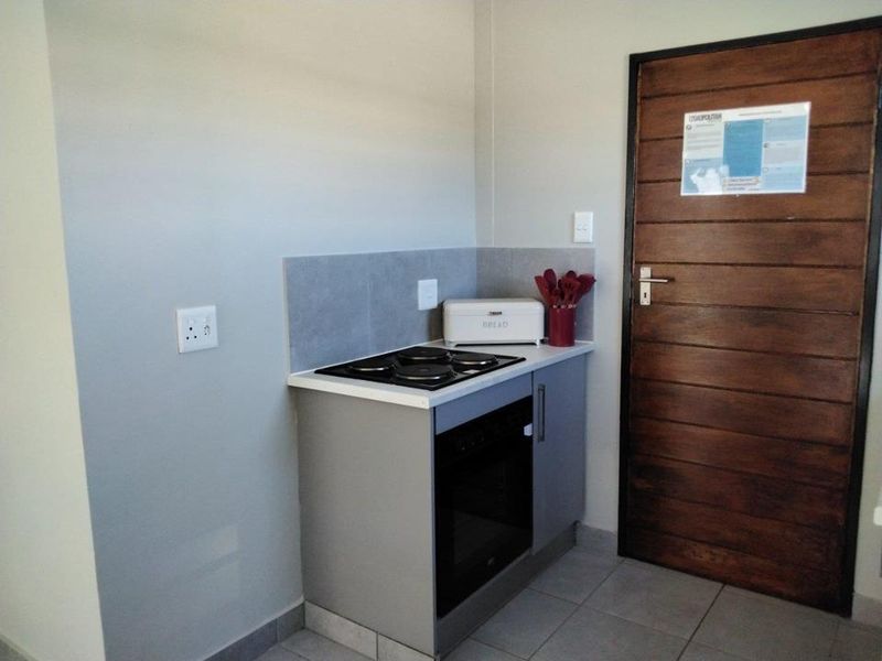 Compact kitchen area featuring a built-in oven, electric hob, tiled splashback, and modern base cabinetry, adjacent to a solid timber door.