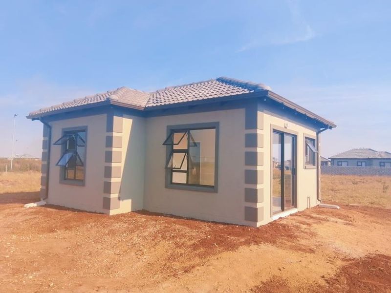 A newly constructed single-story house featuring a tiled roof, plastered exterior walls, and modern aluminium window frames, set on an undeveloped plot.