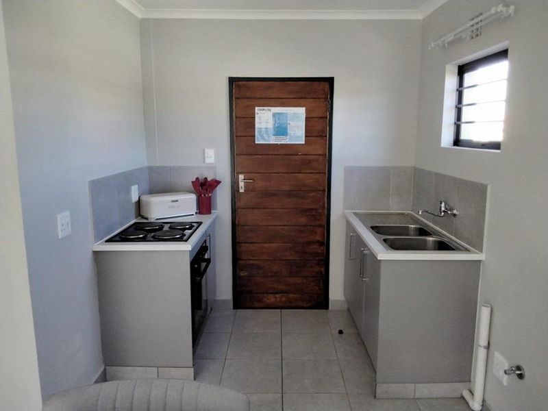Compact kitchen featuring built-in cabinetry, a double sink, a stove with oven, and tiled splashbacks, providing a functional and efficient workspace.