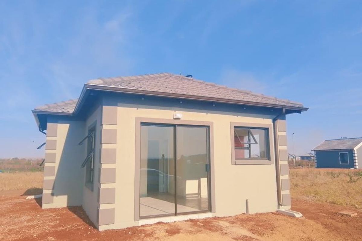 Rear view of a modern single-story house featuring a sliding glass door, casement windows, and a tiled roof set on an undeveloped plot.