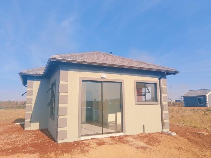 Rear view of a modern single-story house featuring a sliding glass door, casement windows, and a tiled roof set on an undeveloped plot.